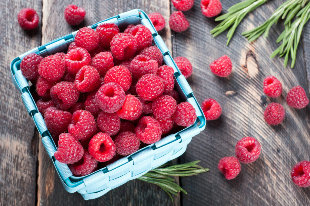 Obrazek świeżych malin dodanych do deseru lub smoothie. Grafika ilustruje, jak maliny wspomagają zdrowie i odchudzanie w diecie pudełkowej dzięki antyoksydantom i błonnikowi. Doskonałe do artykułu o malinach w diecie pudełkowej.